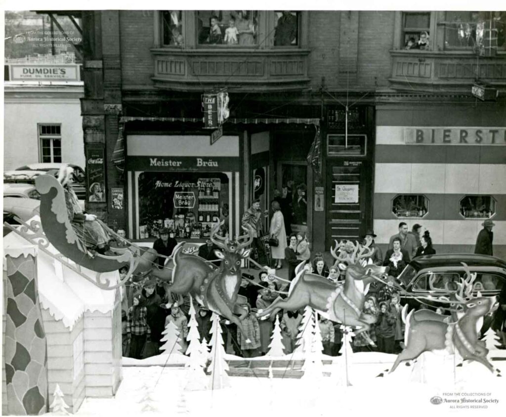 Float from Aurora Christmas Parade travels north on Broadway, north of Benton, passing Home Liquor Store and the Bierstube Bar & Cocktail Lounge, 1949 (Aurora Historical Society photo)